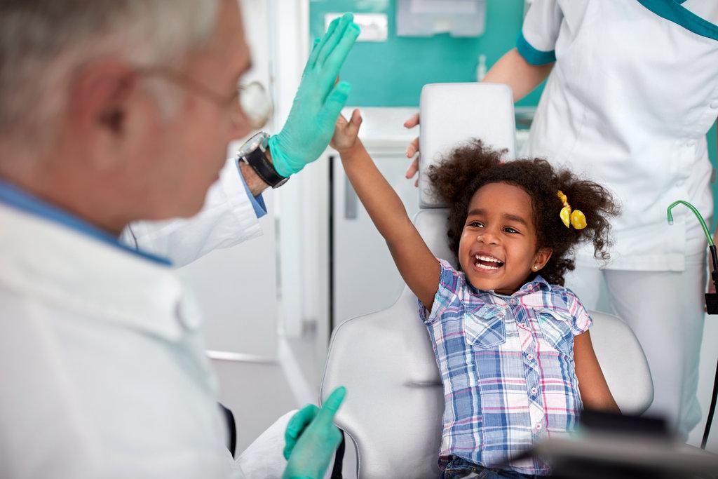Black cheerful young girl in dental chair making joke with male dentist