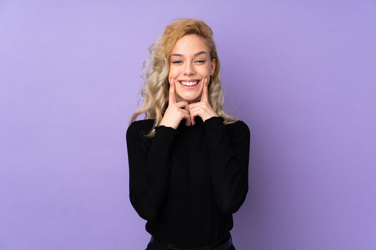 Young blonde woman isolated on purple background smiling with a happy and pleasant expression Young blonde woman isolated on purple background smiling with a happy and pleasant expression
