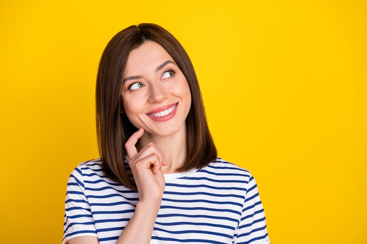 Photo of gorgeous adorable nice girl with brunette hairdo dressed striped t-shirt look empty space isolated on yellow color background Photo of gorgeous adorable nice girl with brunette hairdo dressed striped t-shirt look empty space isolated on yellow color background.