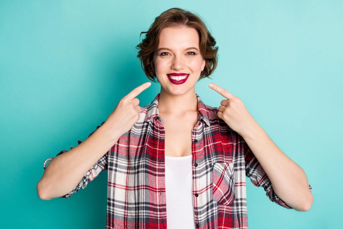 Portrait of positive cheerful girl point index finger on beaming smile show her perfect ideal teeth after medicine clinic wear stylish clothing isolated over teal color background Portrait of positive cheerful girl point index finger on beaming smile, show her perfect ideal teeth after medicine clinic wear stylish clothing isolated over teal color background